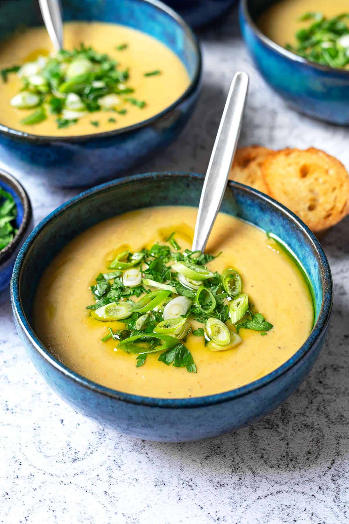 a close up of a bowl of potato soup with a spoon topped with green onions and parsley.