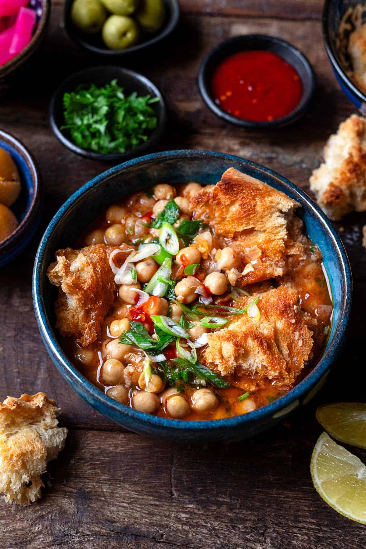 lablabi tunisian chickpea stew in a bowl, next to bowls of various toppings.