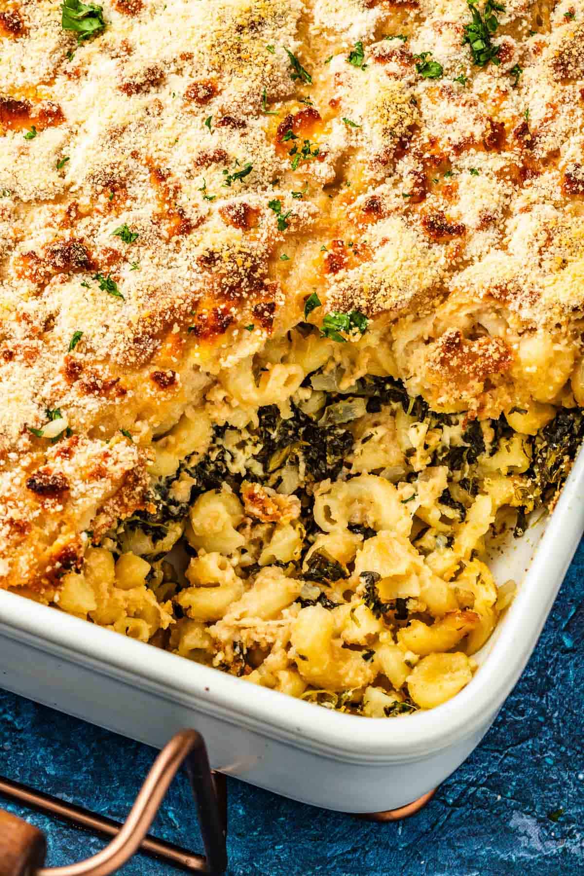 Side shot of Spanakopita Mac and cheese in a baking dish with a piece that has been removed.