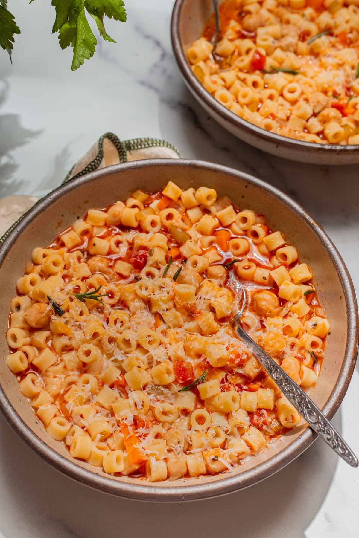 Two bowls of pasta e ceci with rosemary garnished on top.