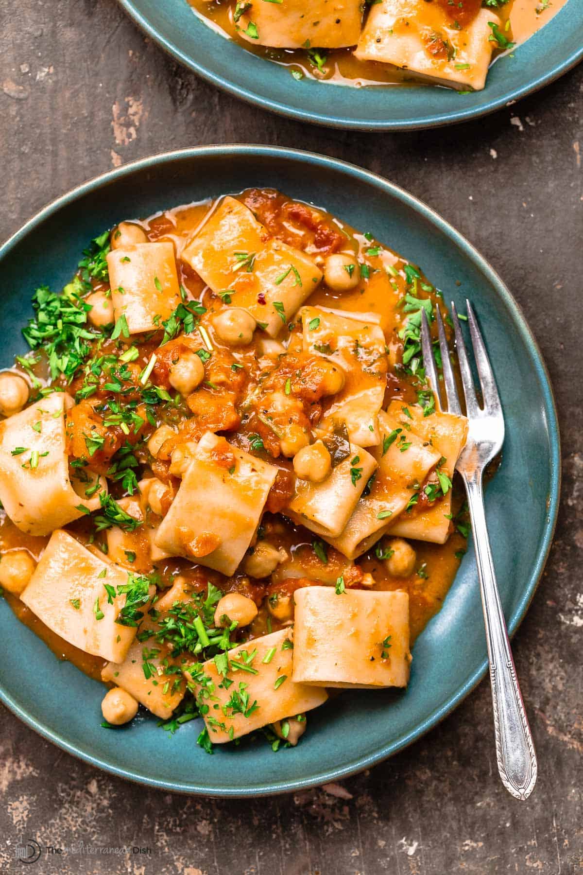 A bowl of creamy tomato pasta with chickpeas, garnished with parsley. Another bowl to the side