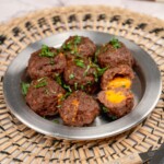 Cheese stuffed meatballs served on a plate and one of them cut open showing the melted cheese inside.