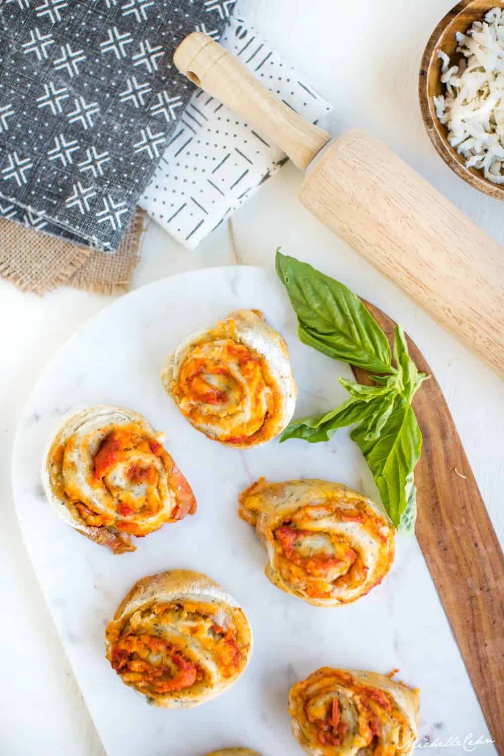 vegan pizza rolls filled with vegan cheese and sauce on a marble surface with marinara sauce in the bottom left corner