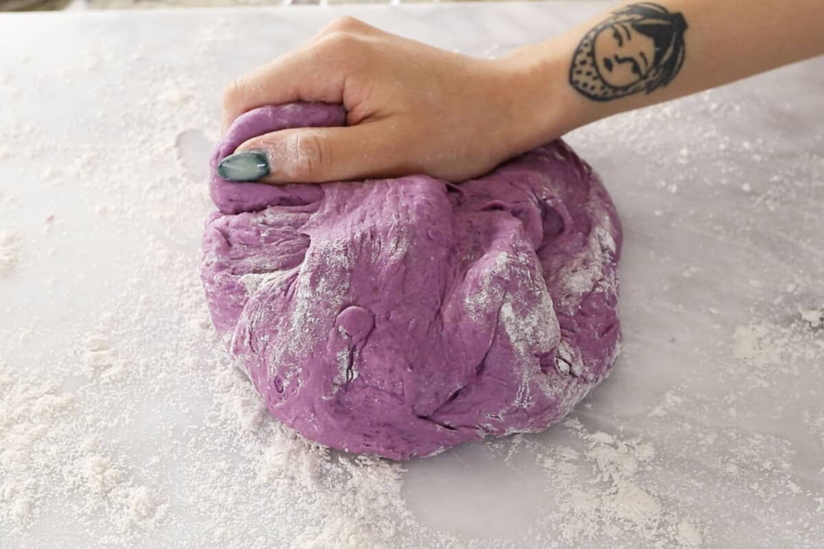 kneading fluffy ube brioche bread dough in large glass bowl