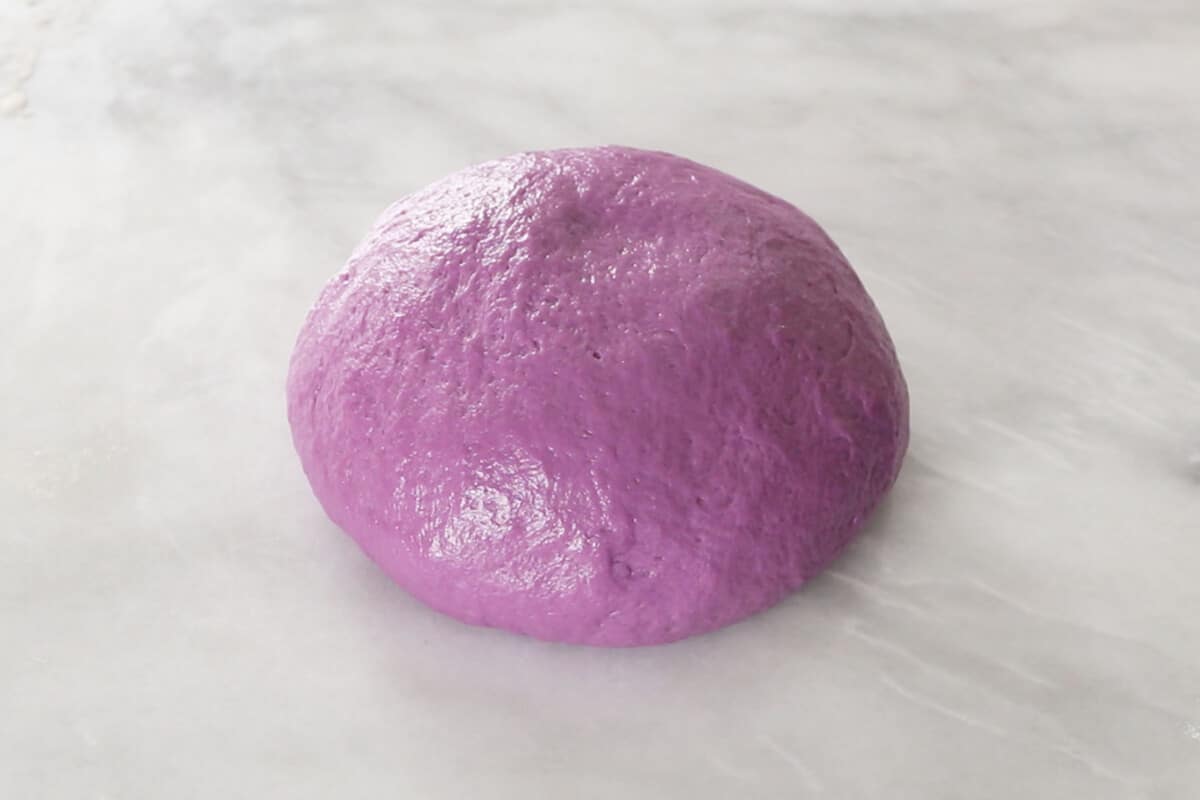 kneading fluffy ube brioche bread dough in large glass bowl