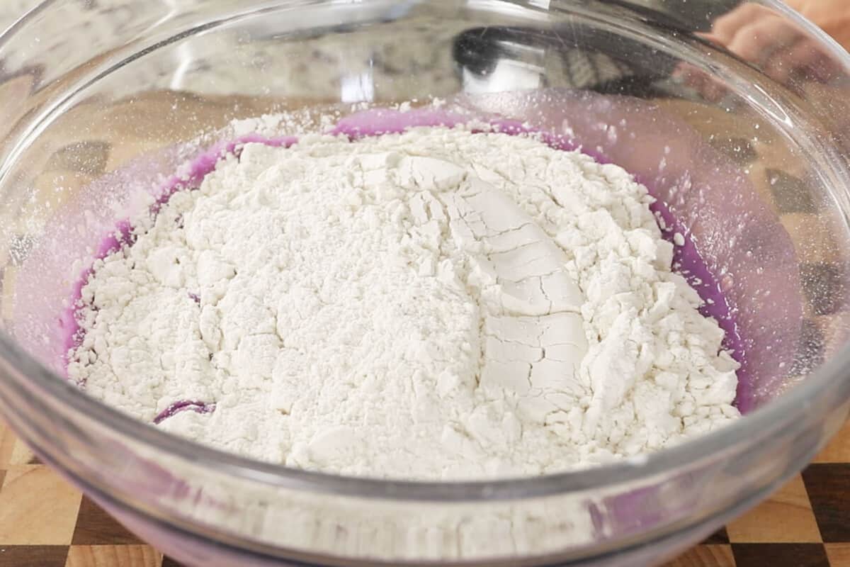 adding flour to fluffy ube brioche bread dough in large glass bowl