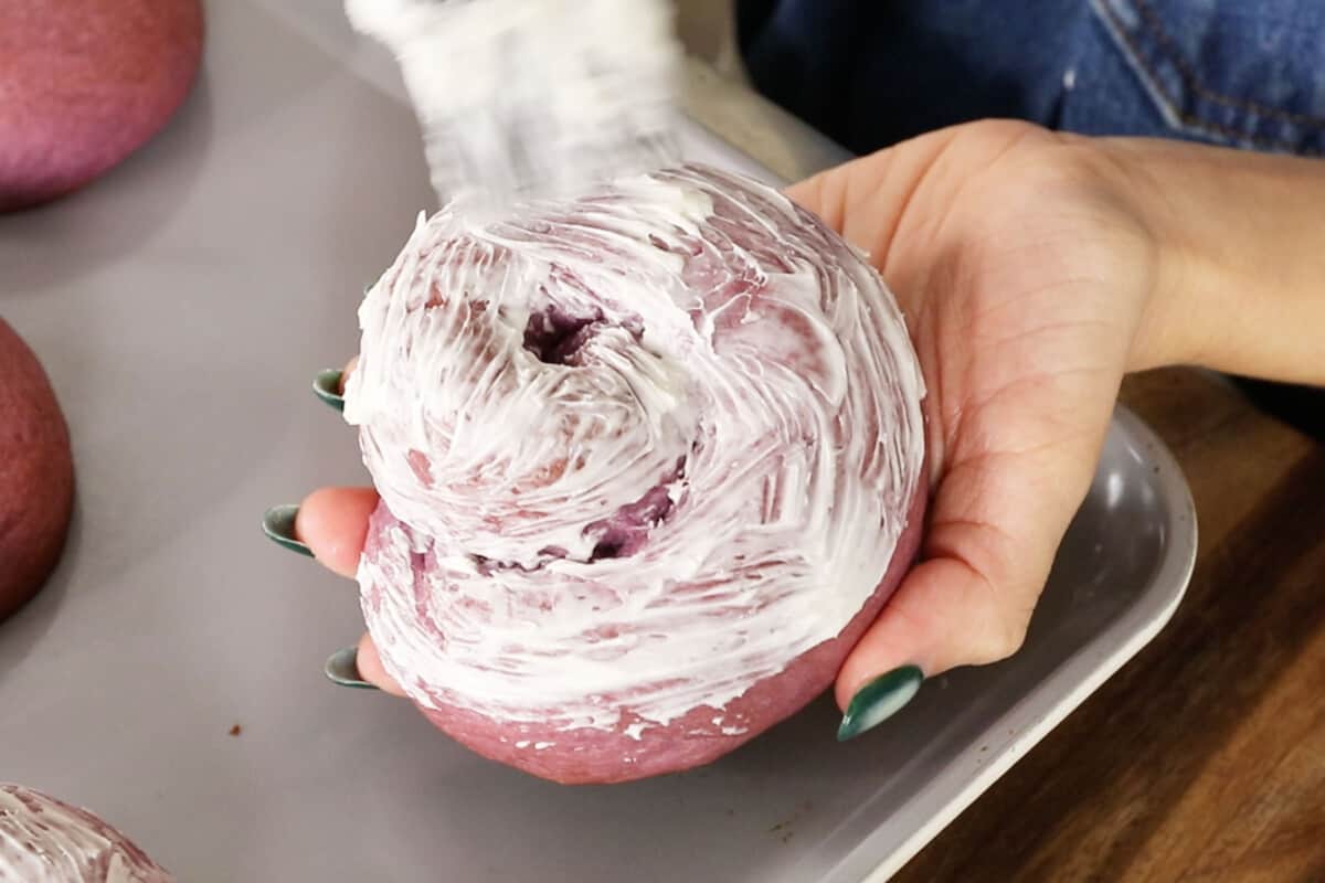 adding buttercream to Filipino ube ensaymada brioche bread