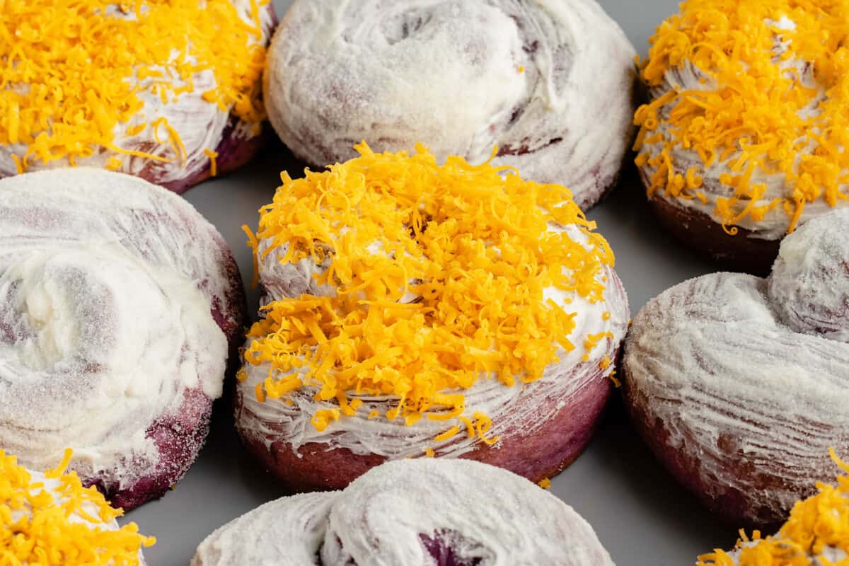 horizontal photo of ube ensaymada with cheddar cheese on a baking sheet