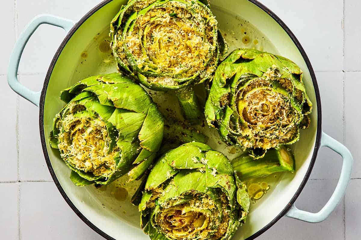 An overhead photo of four uncooked stuffed artichokes in a pot.