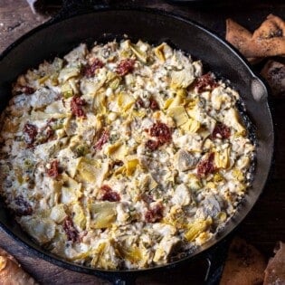 close up of cooked artichoke dip with feta in a cast iron skillet surrounded by fried pita chips.