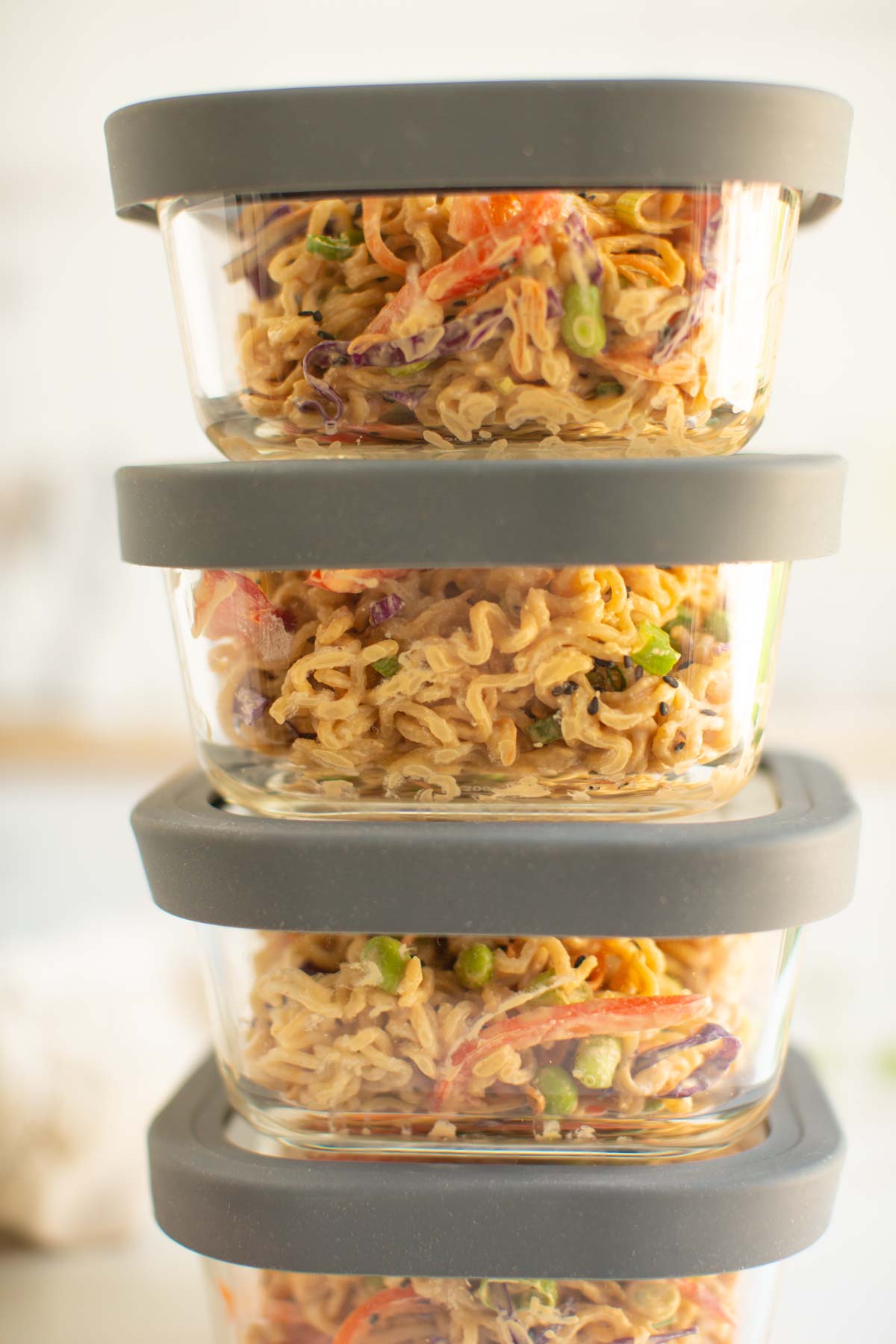 Four glass meal prep containers packed with peanutty ramen noodles with veggies. 