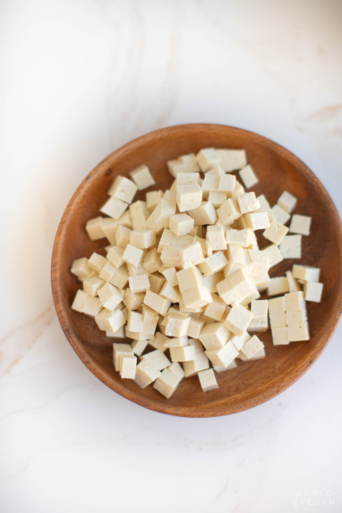 A wooden bowl with finely cubed tofu that can be added for a protein boost.