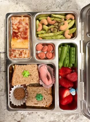 Kids lunchbox featuring pizza, pea crisps, peanut butter and jelly, fruit, peas, and more.