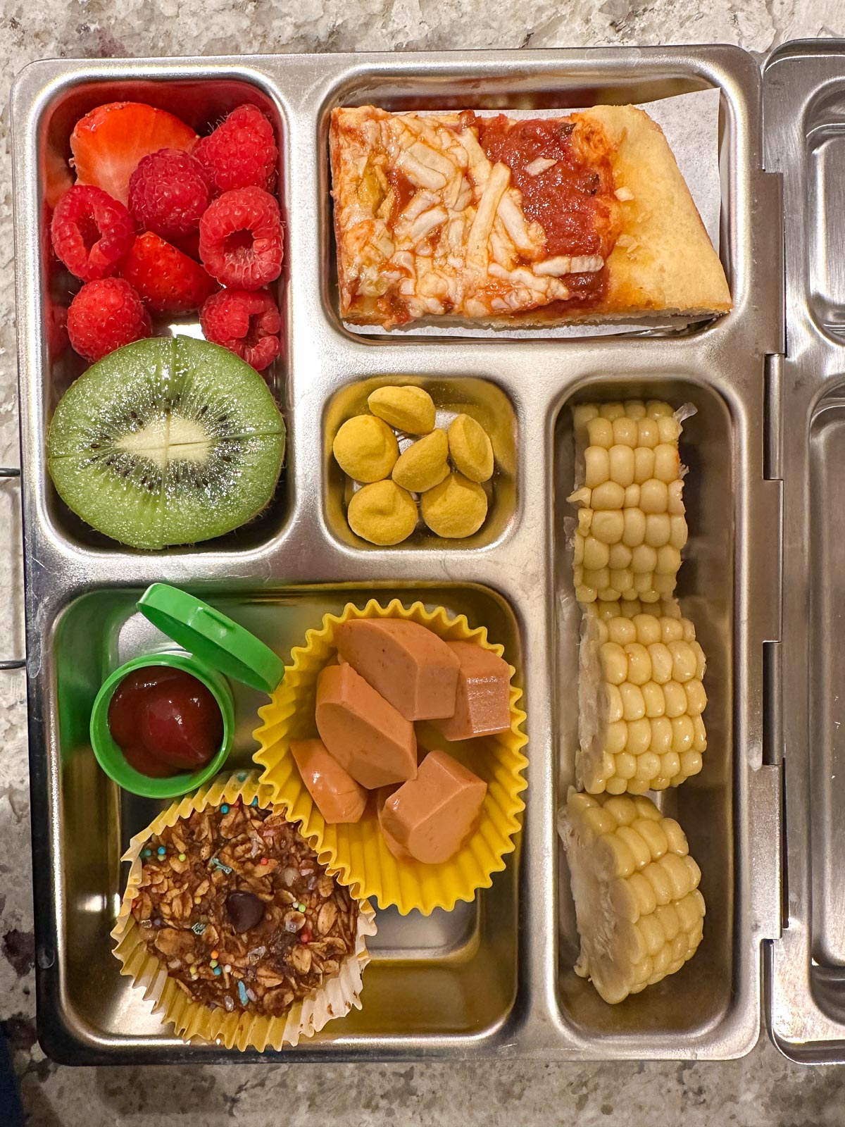 Plant-based kids lunch box with pizza, corn, veggie hotdogs, and more. 