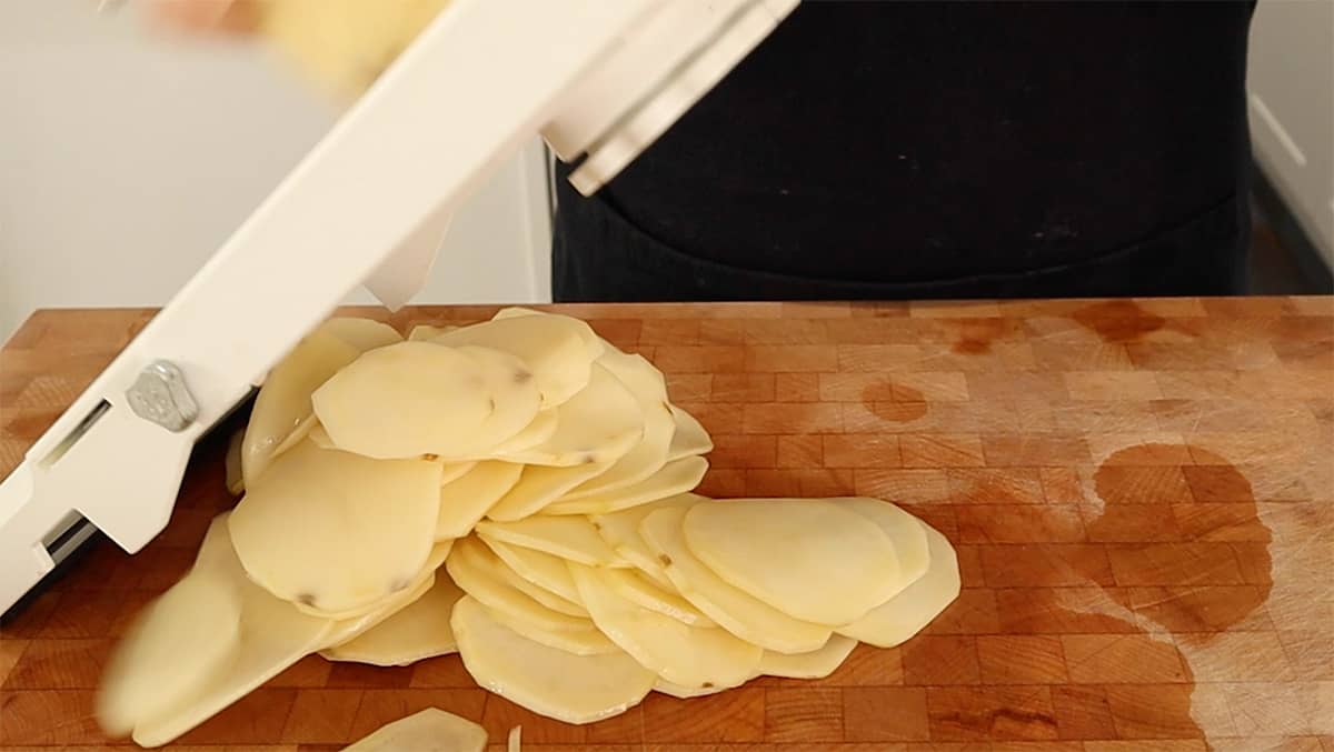 a peeled potato being sliced on mandolin