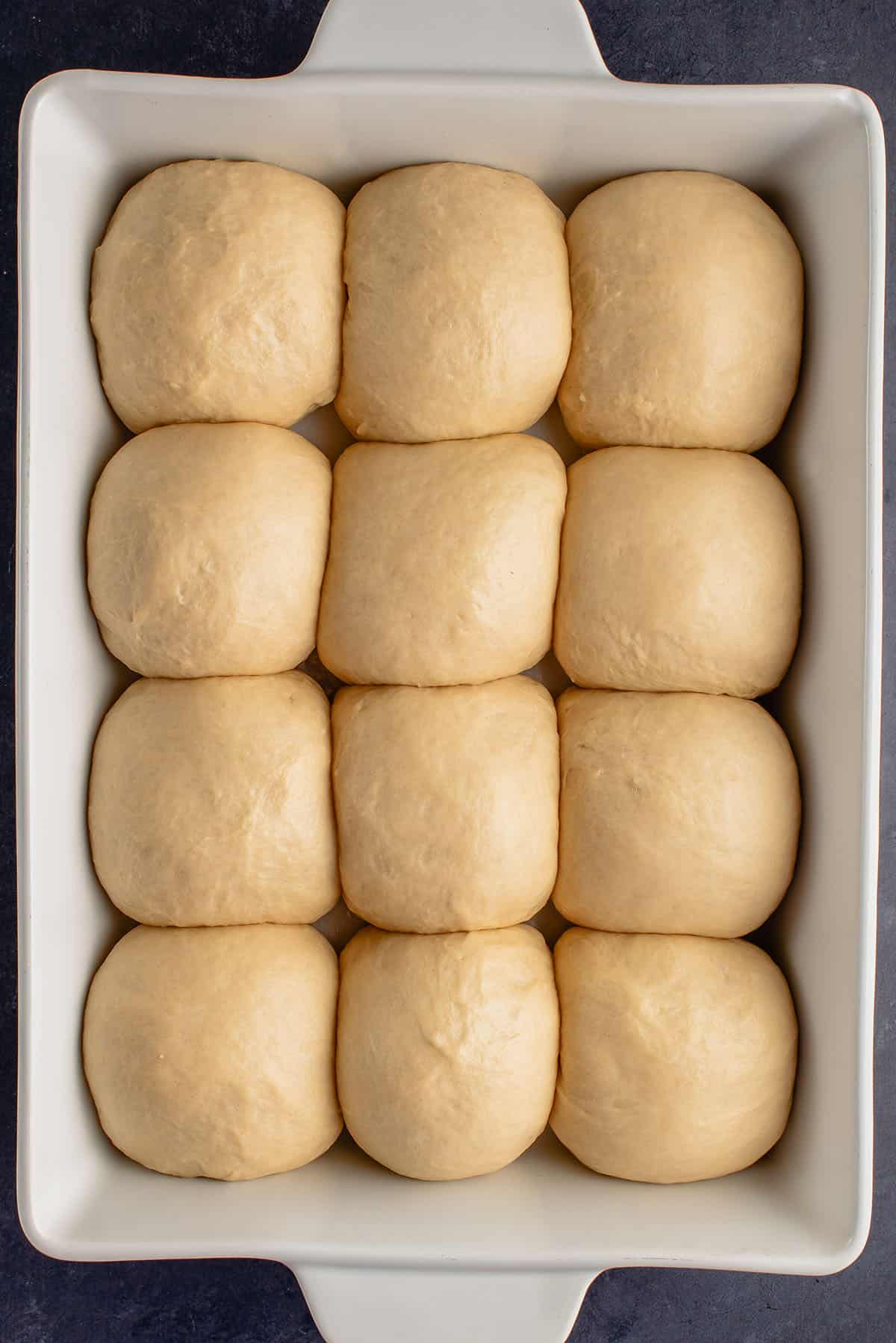 overhead photo of risen vegan Hawaiian rolls in white baking dish