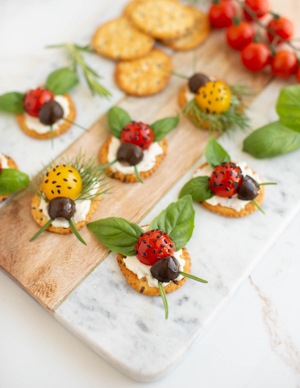 Crackers topped with vegan cream cheese, cherry tomatoes, black olives, basil, and chives to look like ladybugs.