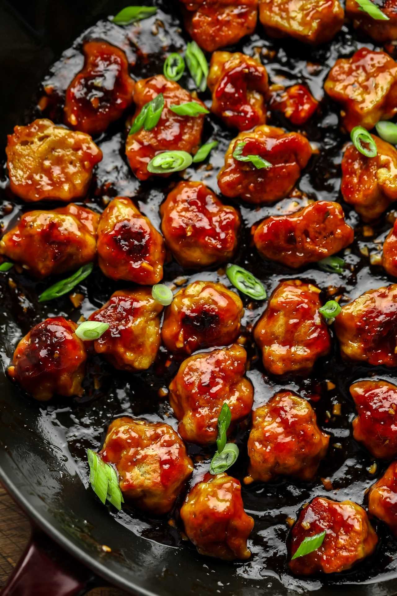 close up on bite-sized seitan nuggets covered in a "honey" ginger sauce and cooking in a large black skillet.