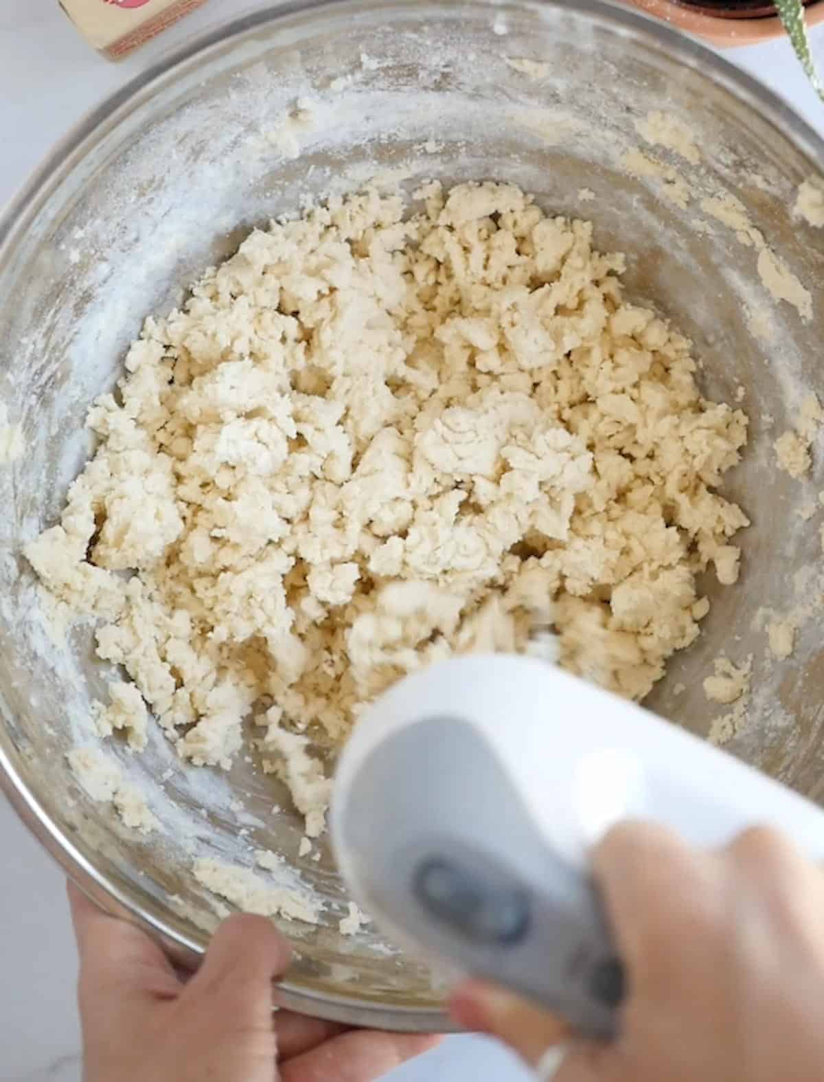 Crumbly shortbread cookie batter that is being mixed with an electric hand mixer.