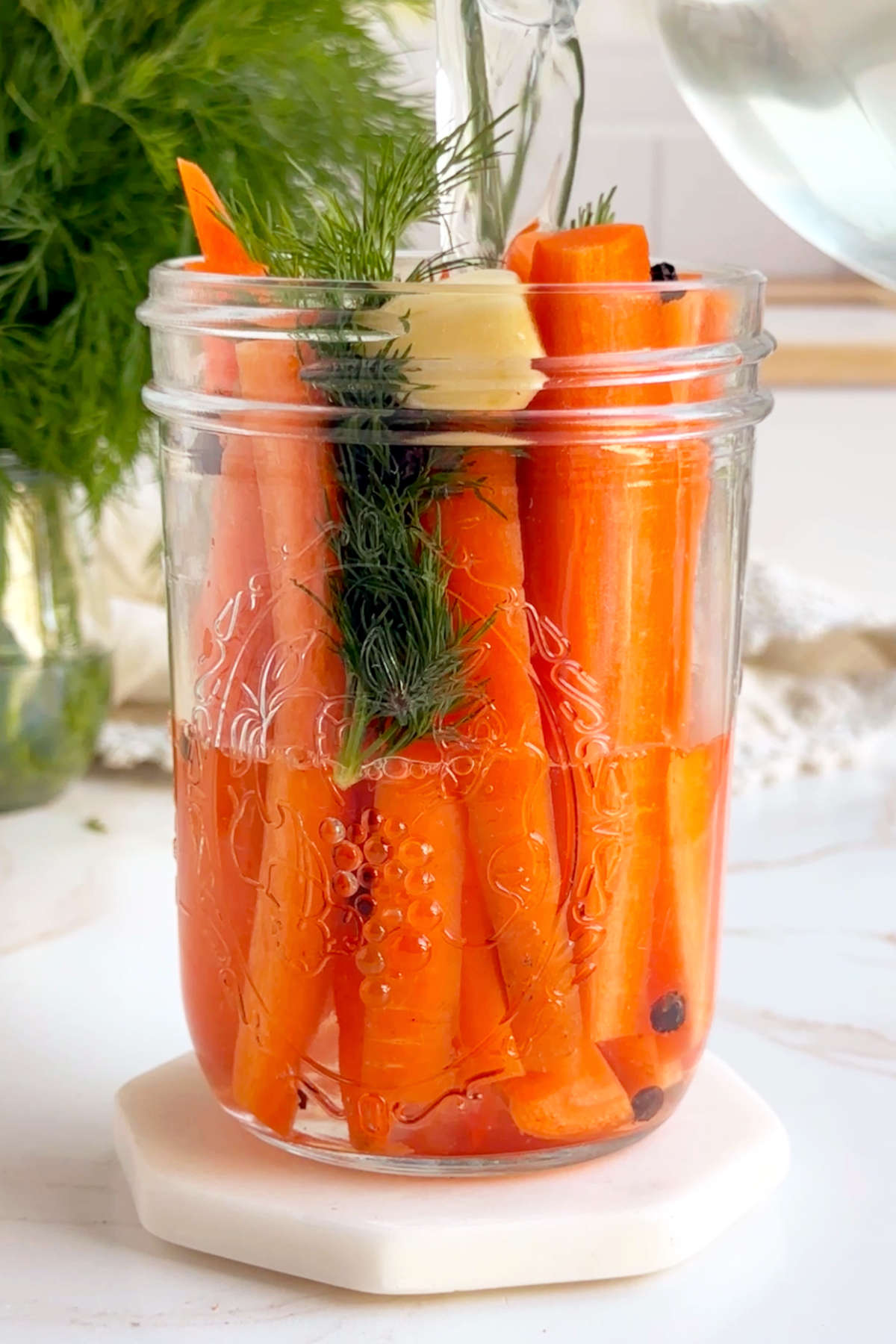 Pickling brine being poured over the carrots and mix-ins in a glass jar.