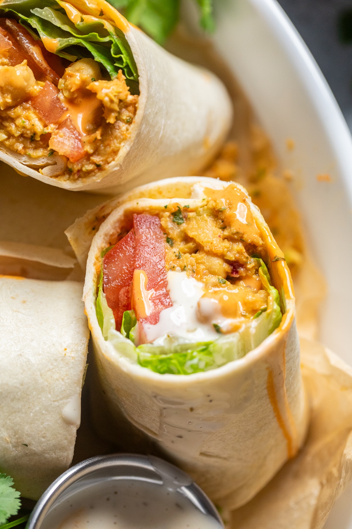 close up of a vegan buffalo chickpea salad wrap with lettuce and tomatoes.