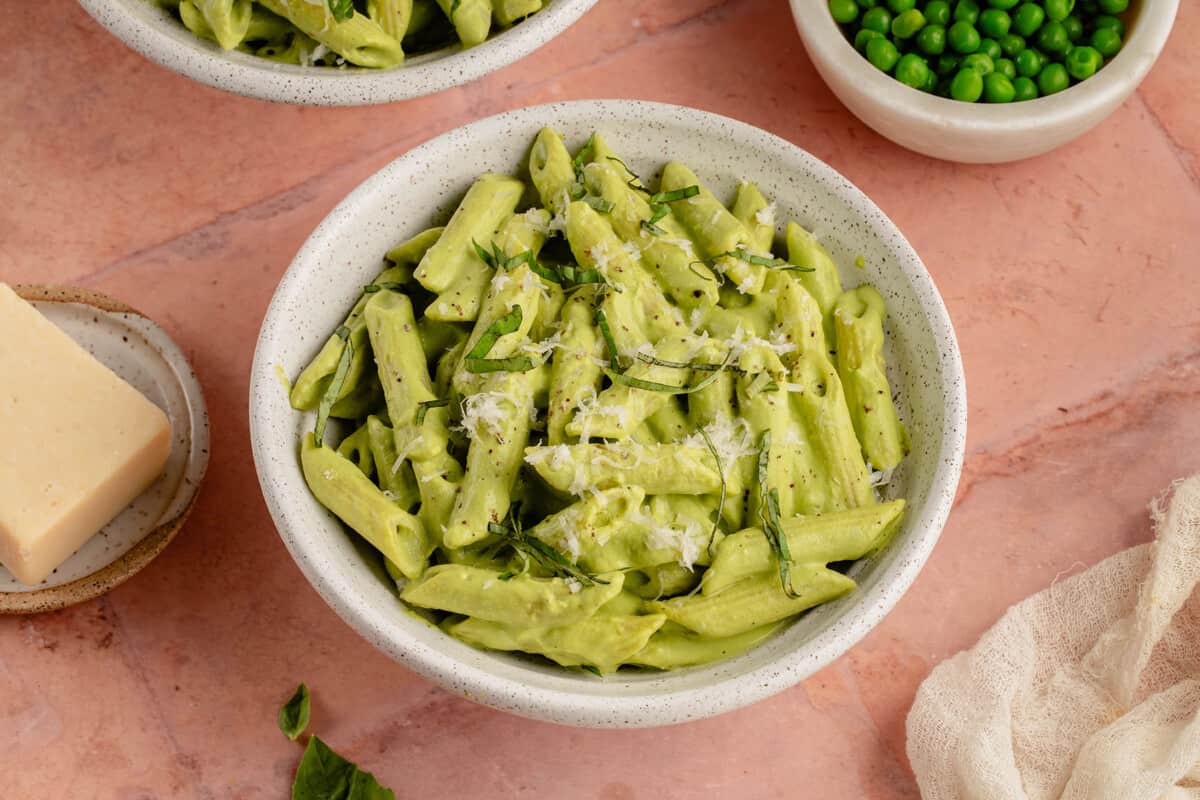 bowl of pea pesto pasta with a side of parm and fresh peas