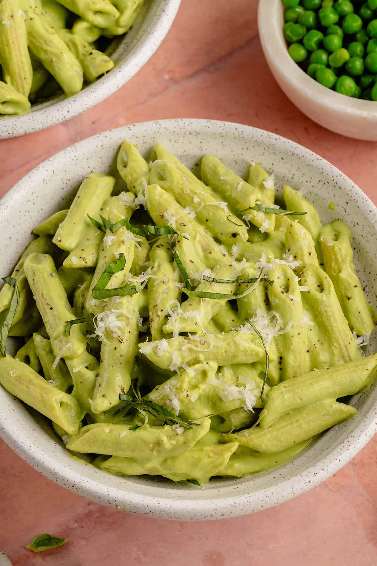 white bowl filled with pea pesto pasta stopped with fresh basil and parm on pink background