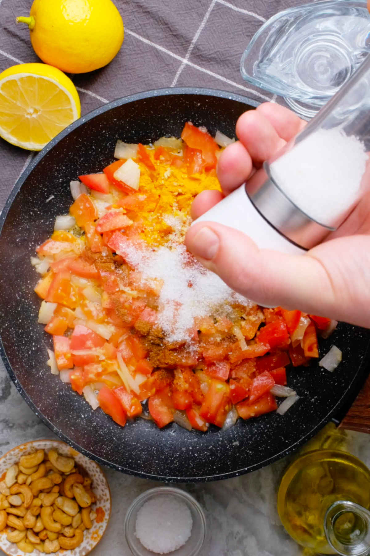 Hands holding a salt shaker over the pan of vegan butter chicken sauce ingredients.