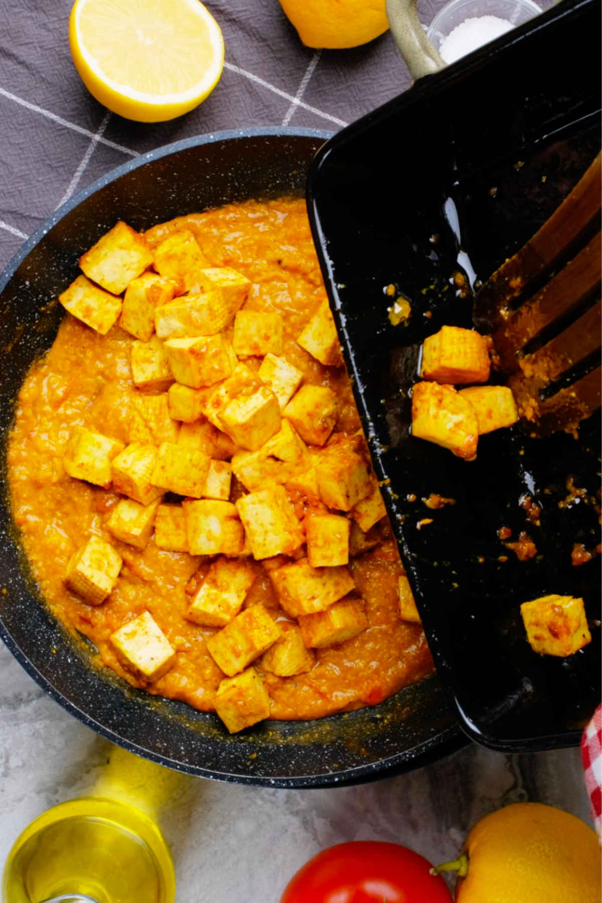 Baked tofu being added to the saucepan of vegan butter chicken sauce.