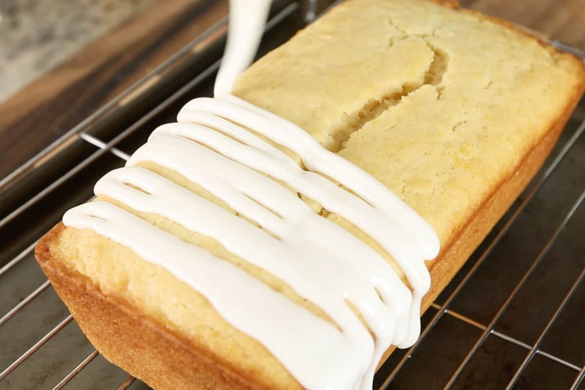 pouring glaze over a vegan lemon loaf on black cooling rack