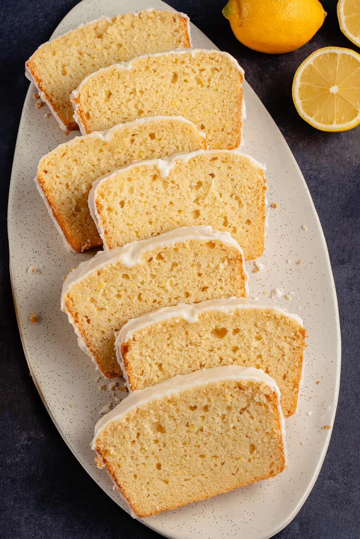 close up photo of 7 vegan glazed lemon loaf slices on white serving tray next to fresh lemons