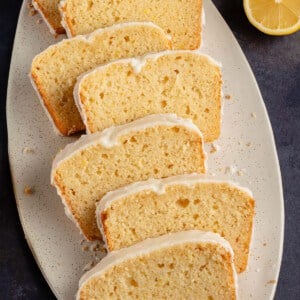 close up photo of 7 vegan glazed lemon loaf slices on white serving tray next to fresh lemons