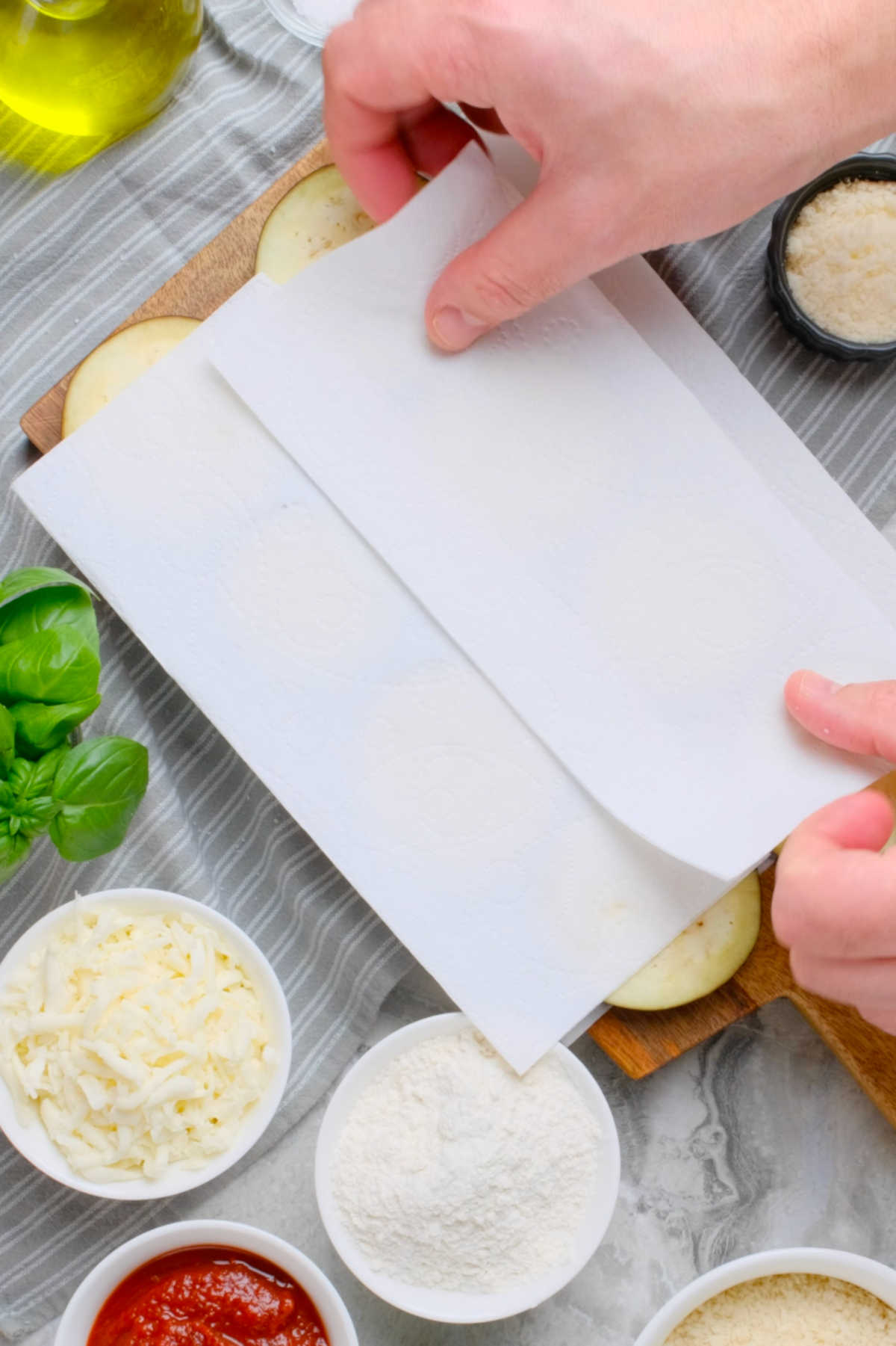 A pair of hands placing paper towels over the eggplant slices.