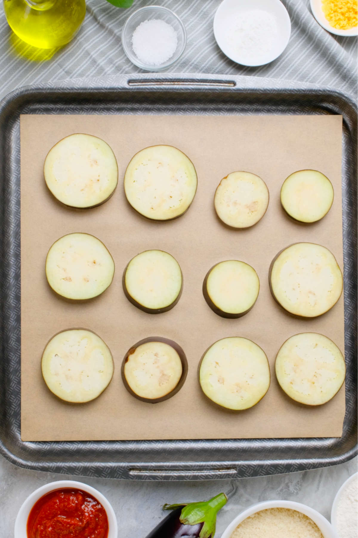 Slices of eggplant spaced out on a baking tray lined with parchment paper.