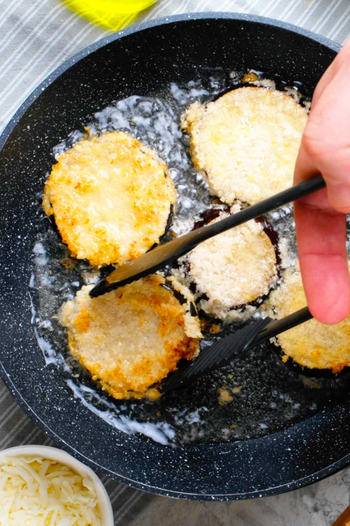 Vegan eggplant parmesan slices frying in a skillet.