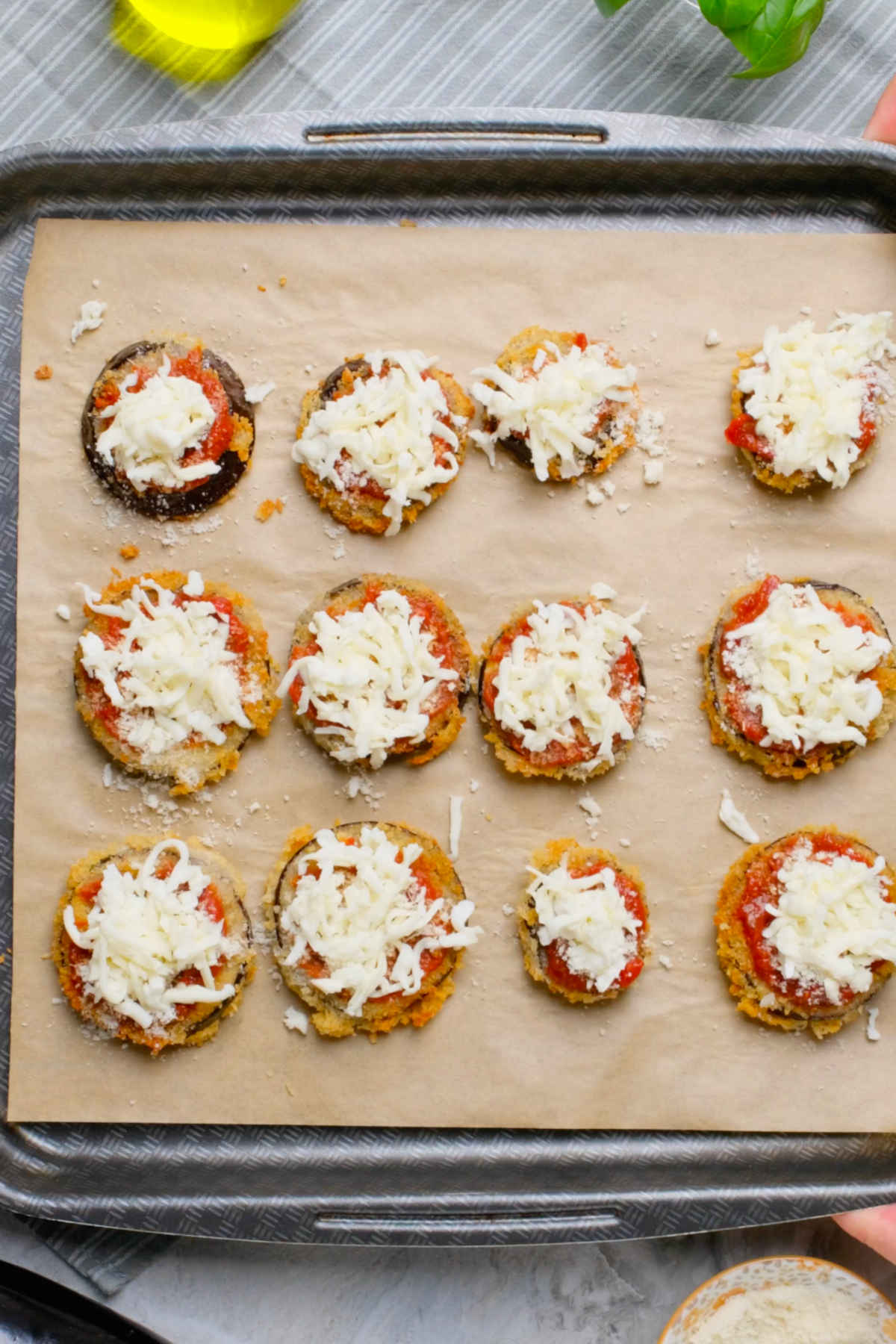 Slices of vegan eggplant parmesan on a baking tray with marinara, parmesan, and mozzarella on top.