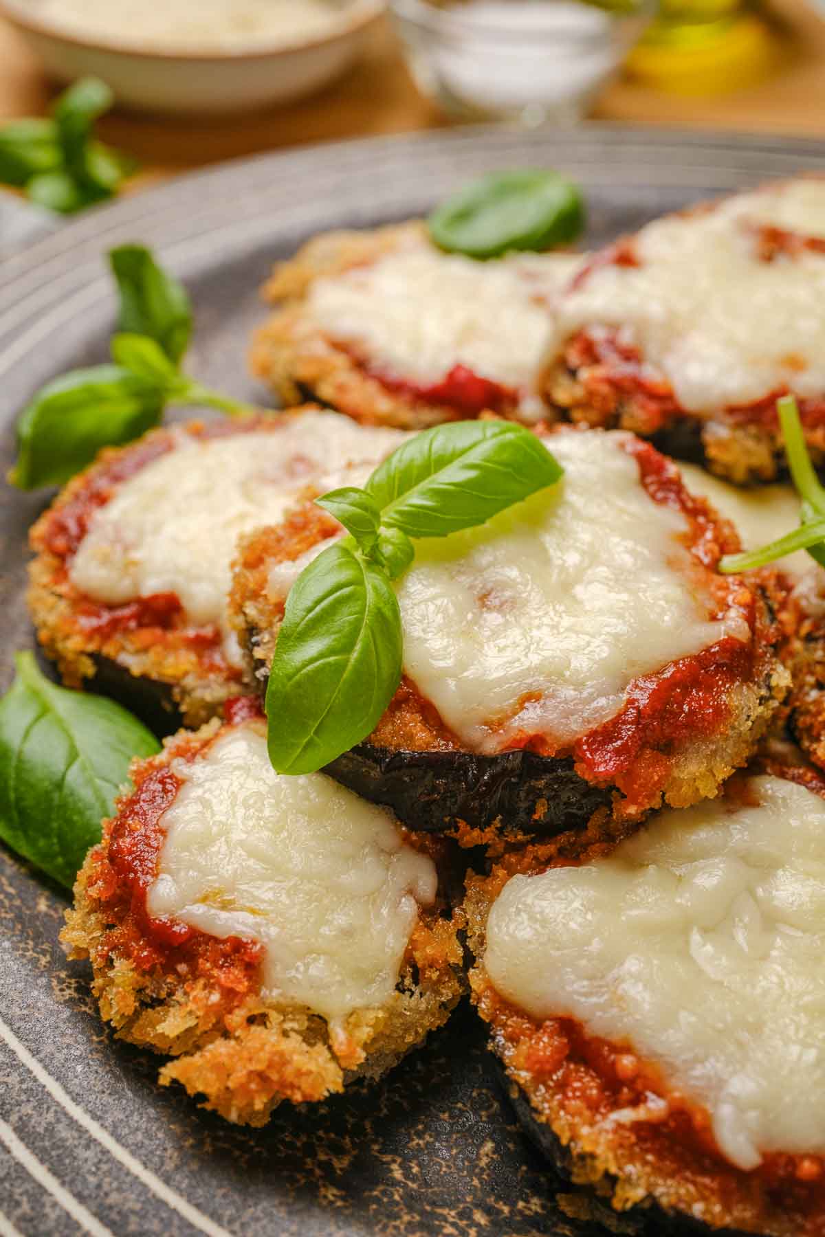 Slices of vegan eggplant parmesan on a plate, topped with fresh basil leaves.