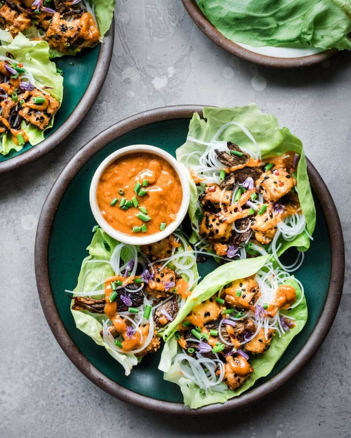 Three lettuce wraps on a plate with dipping sauce.