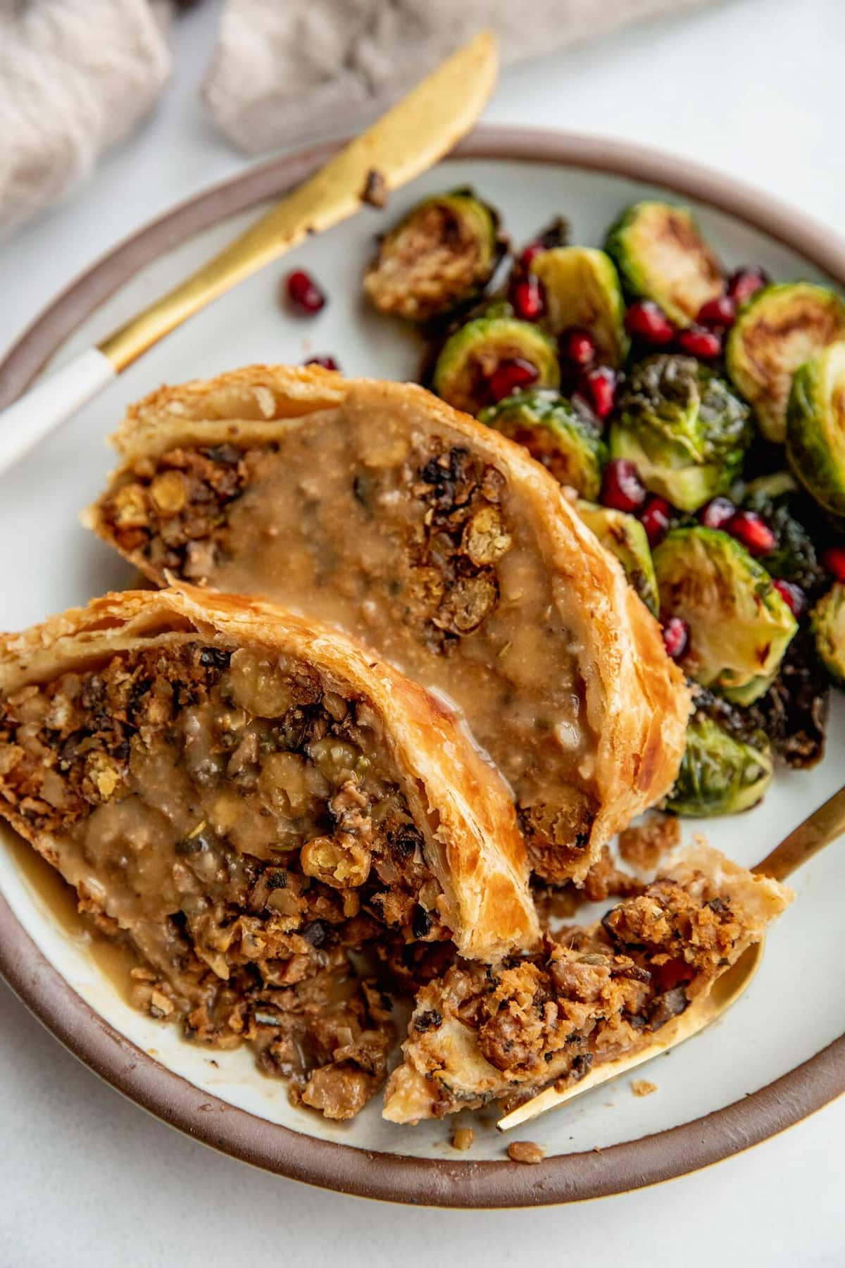 Two slices of mushroom wellington on a plate with roasted vegetables.