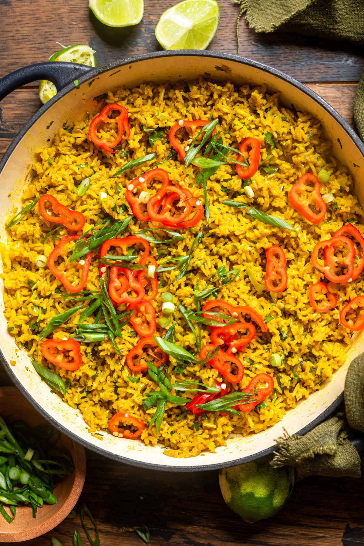 a white pot of garlic turmeric rice atop a table with red chilis and green onions garnished on the top.