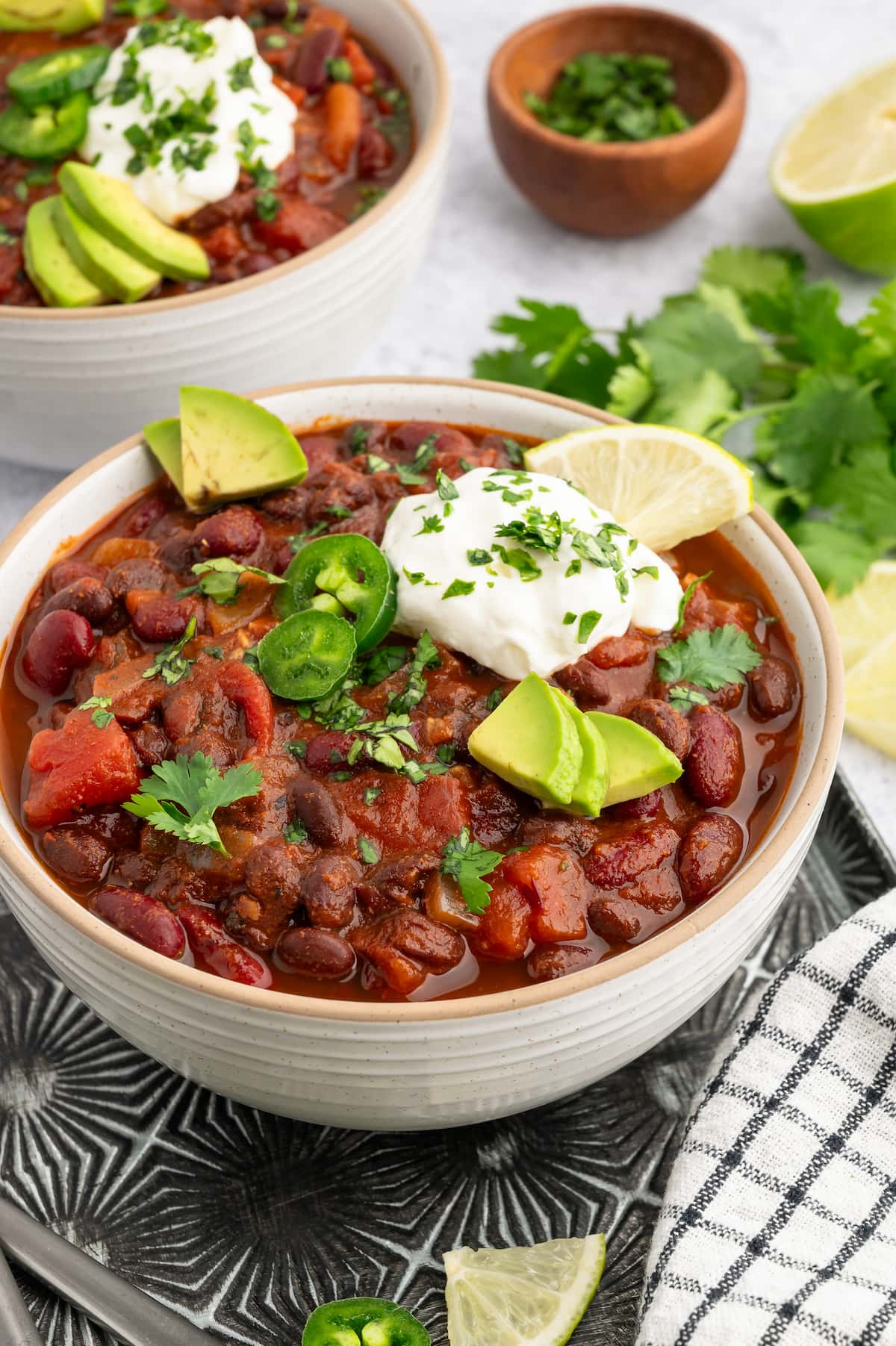 Vegan chili in a bowl topped with cilantro, vegan sour cream, jalapeno and avocado slices.