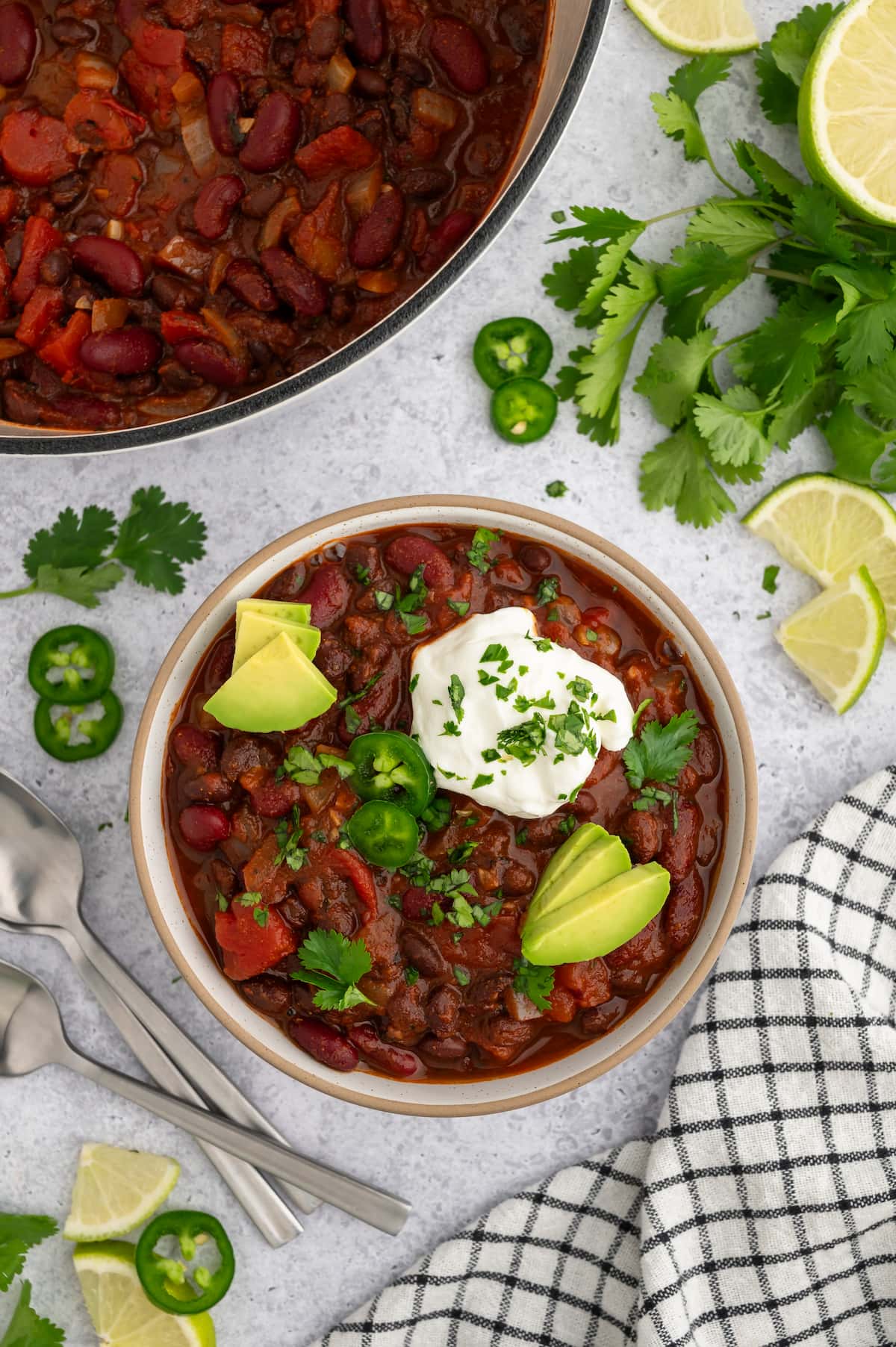 A bowl of vegan chili with toppings, next to a large pot of chili.