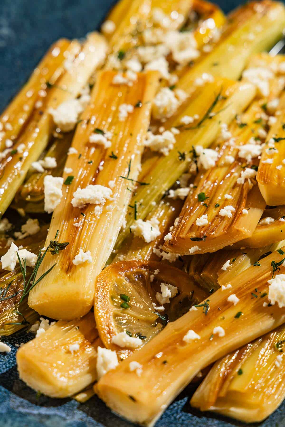 A close up photo of braised leeks garnished with dill and crumbled feta.