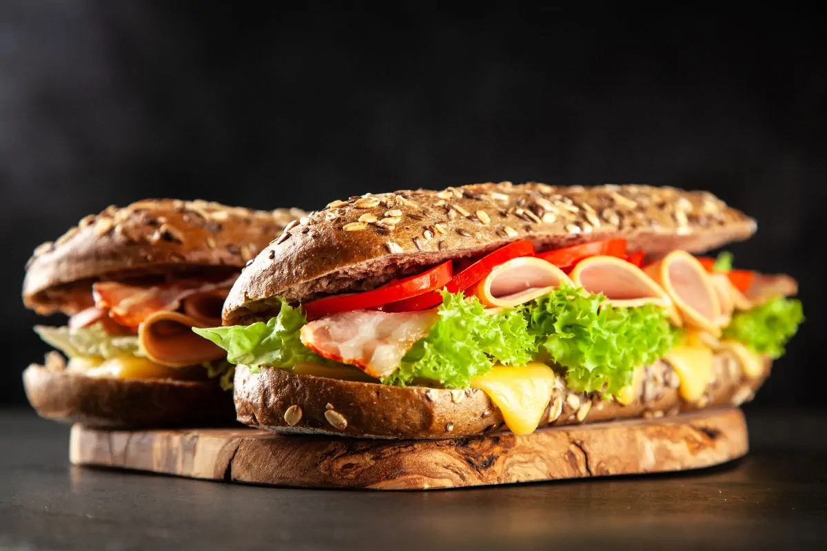 A sandwich revealing the filling of melted cheese, lettuce, ham and sliced tomatoes.
