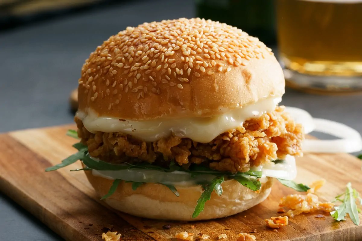 A close up shot of chicken burger with sesame bun and melted cheese.